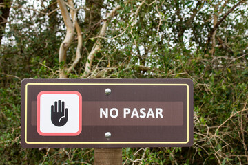 Fototapeta premium Sign that reads “NO PASAR” with stop hand symbol in a natural forest setting