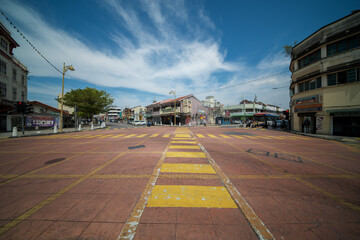 Obraz premium Wide-angle shot of an empty street intersection with a zebra crossing under a bright blue sky with clouds.
