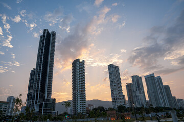 Naklejka premium Dramatic cityscape at sunset with tall skyscrapers silhouetted against a colorful sky.