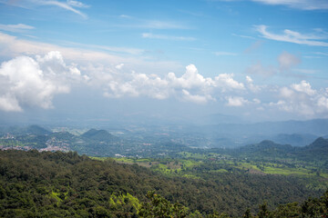 Panoramic view of a lush green valley and distant mountains under a blue sky with scattered clouds.