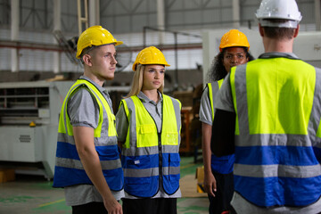 Group of diverse industrial workers in safety vests and helmets listening to supervisor during briefing at factory, showing teamwork, training, discipline and communication in workplace safety.