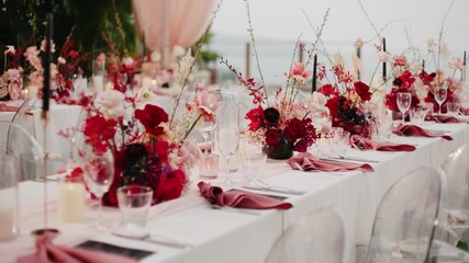 Luxurious wedding table decorated with vibrant red and pink floral arrangements, elegant glassware, and folded napkins, creating a romantic and festive celebration atmosphere.