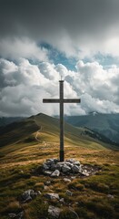 Wooden cross stands atop a grassy mountain peak, with cloudy skies and distant mountains in the background.