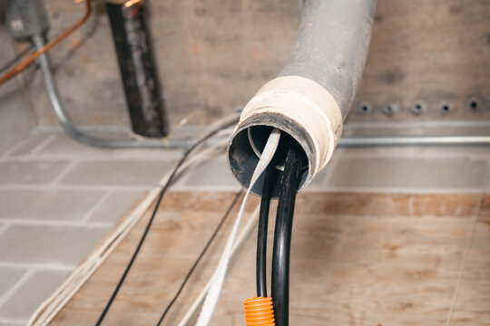 Conduit pipe with string and fiber optic cables on ceiling. Close up. Installation to fiber optics in building electrical room. High-speed internet upgrade or telecom infrastructure. Selective focus.