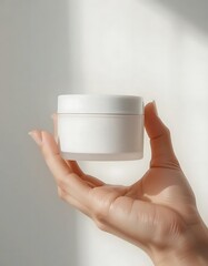 Minimalist skincare product mockup a female hand holding a white blank cosmetic jar . Isolated on white with soft studio lighting. Clean, modern and commercial composition. Perfect for beauty branding