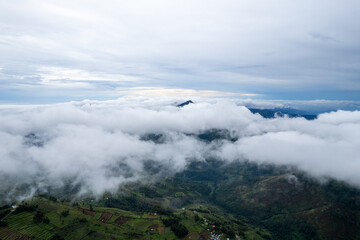 Aerial view of mountain peak above cloud. Majestic nature landscape with summit poking through fog and mist over green valley
