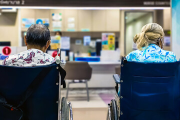 Back view of Elderly male patient sit on wheelchair waiting to see doctor in health care office or hospital. Patients sit on wheelchairs waiting to see doctor in front of examination room in hospital.