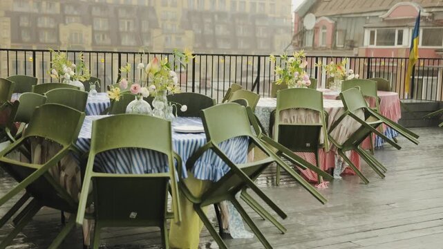 Rain on the cafe terrace. Rainy terrace of a restaurant with tables decorated with flowers and chairs, which is closed due to bad weather.