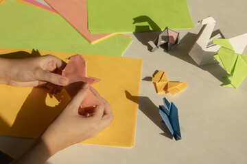 Hands folding colorful paper animals on a table with various origami figures and sheets of paper