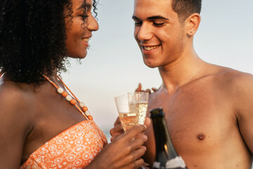 Romantic couple celebrating with a champagne toast on a beach at sunset. Happy young man and woman in love on a summer vacation. Concept of honeymoon, anniversary, and special occasion.