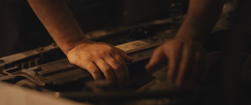 Gritty close-up of a car engine at night, a hand working on the dimly lit mechanical parts