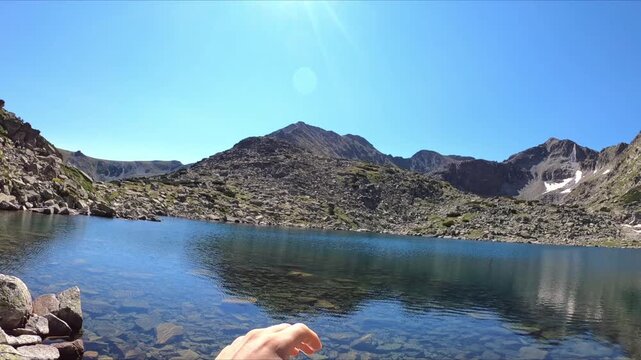 A hand reaches toward the bright sun over a mountain lake on a clear day. Sunshine and landscape idea. Nature and adventure concept.