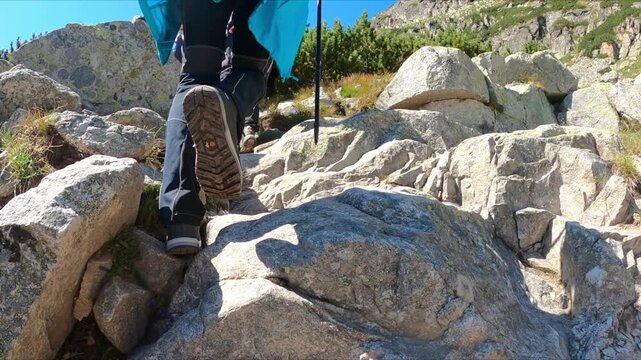 Slow motion of the hikers climb a steep rocky trail in the mountains using trekking poles. Hiking and adventure idea. Nature and outdoor concept.