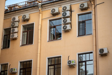 Fototapeta premium Facade of building with many air conditioners on windows in southern hot country. Yellow house exterior on city street. Escape from heat, creating favorable microclimate in urban apartments concept.