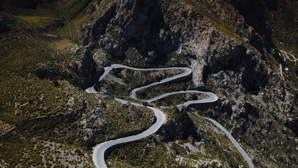 Aerial view of winding mountain road with sharp curves cutting through rocky hills. Scenic serpentine highway surrounded by rugged terrain and wild vegetation.