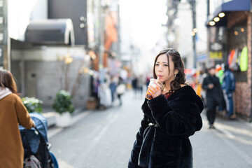 都会の路地でドリンクを楽しむ若い日本人女性