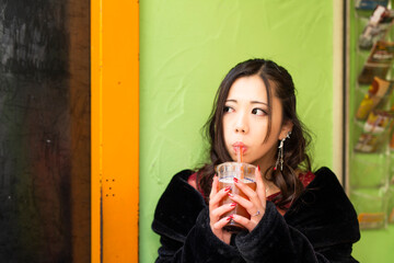 都会の路地でドリンクを楽しむ若い日本人女性