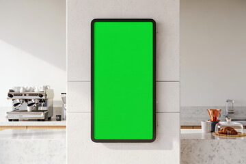 A digital tablet with a green screen mockup hanging on a wall in a modern cafe or kitchen interior.