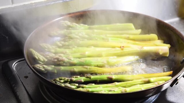 Close-up of asparagus being steamed in a hot pan with water and stirred by a wooden spatula. Healthy cooking and vegetable recipe idea. Fresh greens and gourmet side dish concept.