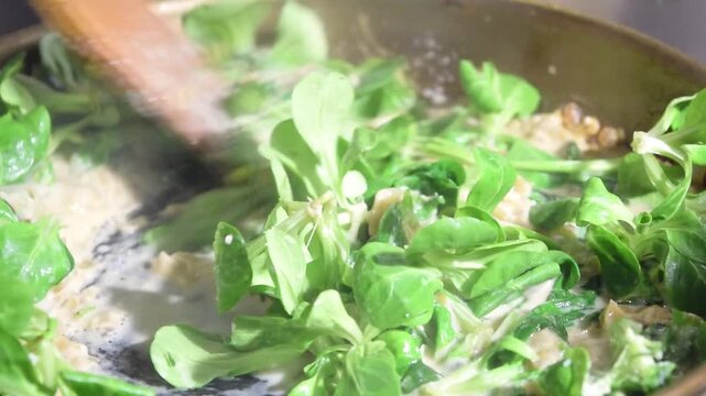 Close-up of fresh spinach being mixed in a hot pan with onions and sauce. Healthy cooking and vegetable recipe idea. Green food and gourmet meal concept