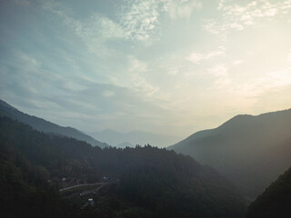 Fototapeta premium A serene landscape featuring mountains and a valley shrouded in mist. The sky is pale with wispy clouds, hinting at sunrise. A winding road cuts through the valley.