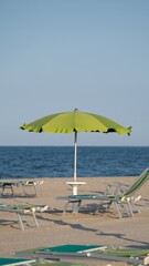 Green beach umbrella and loungers on empty summer coastline