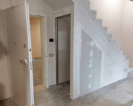 Workers renovating a house using plasterboard and stucco under the stairwell