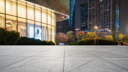 Modern city square with glass building and tall skyscrapers at night © zhouyilu