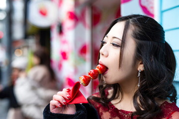 都会の路地でいちご飴を食べる日本人女性のポートレート