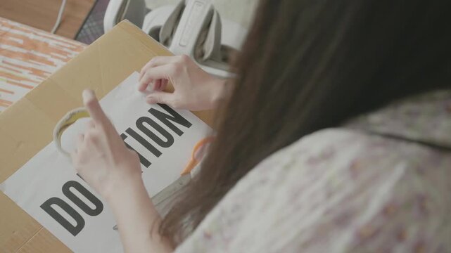 A close-up view of a person holding a sign that reads "Donation" while interacting with a donation box, emphasizing community involvement and support.