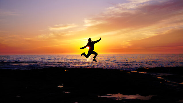 Joyful silhouette leaps across the ocean at sunset person jumping