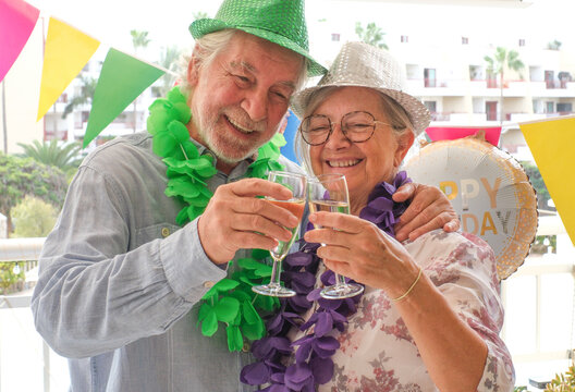 Joyful elderly couple celebrates a birthday in a festive and colorful setting. Wearing party hats they share a birthday cake marked with candles shaped “75,” surrounded by balloons and decorations - Powered by Adobe