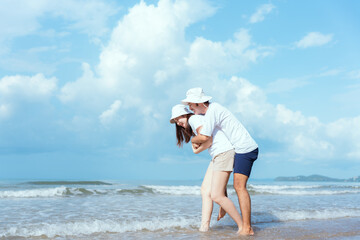 Couple walks hand in hand along a serene beach shoreline during the day under fluffy clouds