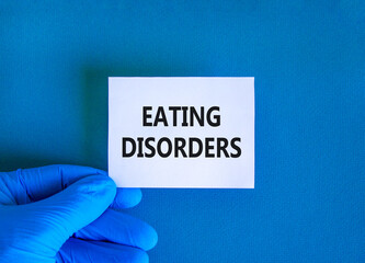 Eating disorders symbol. Concept words Eating disorders on beautiful white card. Doctor's hand in blue medical glove. Beautiful blue background. Medical healthy lifestyle eating disorders concept.
