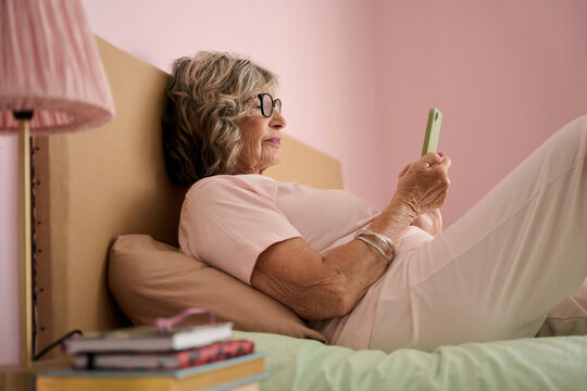 Senior woman using smartphone in bed: relaxing at home