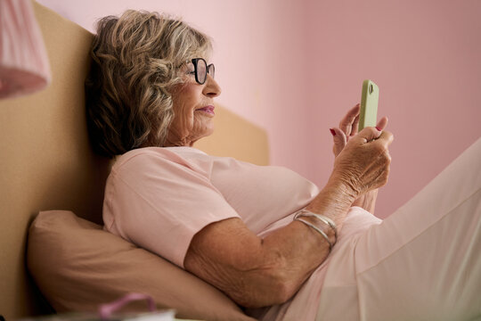 Senior woman using smartphone in bed: relaxing with technology