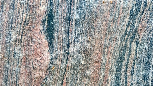 Closeup of the texture of raw granite with stripes of pink, greay and black.  Background
