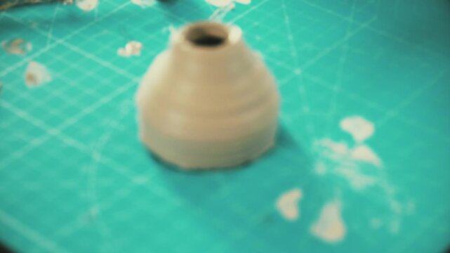 Close-up of hands detaching a freshly shaped clay piece from a small pastel pottery wheel, delicate ceramic work in progress