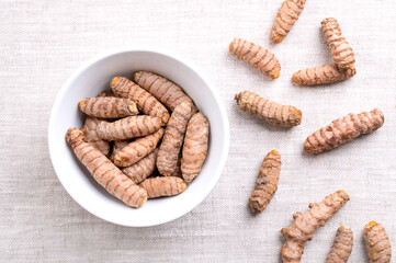 Fresh turmeric rhizomes, in a white bowl, on linen. Underground stems of the turmeric plant Curcuma longa, with bright orange flesh. Used fresh, or dried and ground as turmeric powder. Food photo.