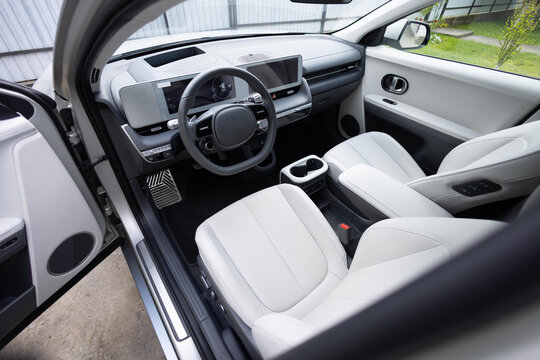 Steering wheel of a electric vehicle, interior cockpit, electric buttons, digital speedometer, front seats, textile, windows, console, gear shift. Car dashboard with a digital touchscreen