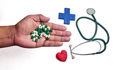 Hand with capsules next to a blue cross and a stethoscope with a red heart, isolated on white background.