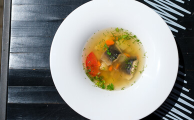 Fish soup with pieces of eel. White plate with wide edges. Black wooden table. Top view. Copy space.
