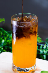 Iced orange coffee in a tall glass, layered with espresso over bright orange juice, served with ice cubes for a refreshing drink.