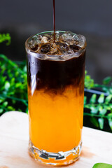 Iced orange coffee in a tall glass, layered with espresso over bright orange juice, served with ice cubes for a refreshing drink.