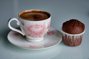 Coffee and chocolate muffin on a white table with floral patterns in a cozy setting for a delightful afternoon treat
