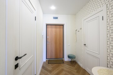 modern entryway with herringbone wood floors, light walls, a wood door, and white paneled doors. A small teal stool adds a pop of color