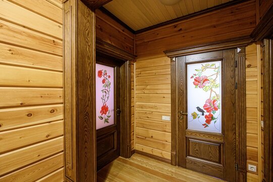 wooden hallway with two decorated doors, one with red roses on pink glass, the other with vibrant flower art and a bird. The walls and ceiling are wood paneled. - Powered by Adobe