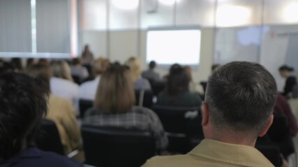 Man is sitting in a classroom with many other people. The man is looking at a projector screen - Powered by Adobe