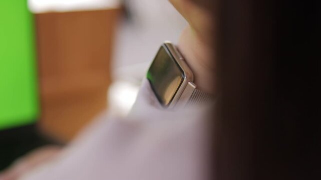 Person wearing a watch with a green background. The watch is silver and has a black face