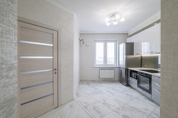 bright kitchen with white cabinets, stainless steel appliances, and light gray, patterned floor tiles. A door with silver accents is visible
